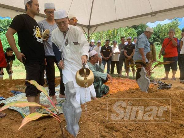 Azih menyiram pusara ibunya yang selamat dikebumikan jam 11 pagi tadi di Tanah Perkuburan Kampung Padang Machang, Manir. -Foto Ihsan pembaca