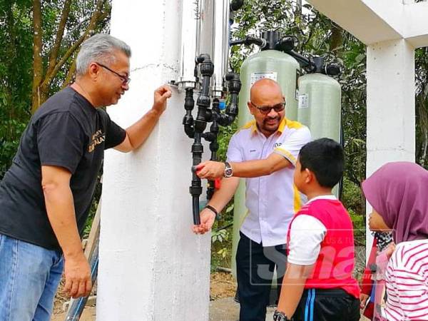 Zafri (kanan) bersama Zawahir (kiri) menunjukkan bekalan air bersih yang ditapis menerusi projek Bekalan Air Bersih Etiqa kepada kanak-kanak di Kampung Padang Bukit, Lubok Setol.