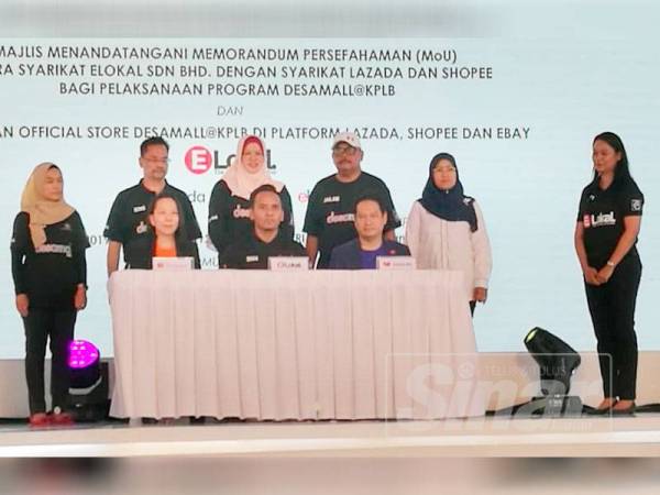 Rina (berdiri, tiga dari kanan) menyaksikan majlis menandatangani MoU antara ELokal Sdn Bhd, Lazada dan Shopee di tapak KUD 2019 di sini hari ini.