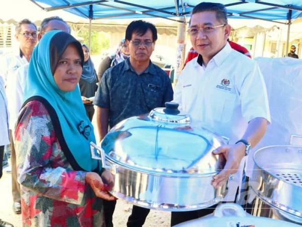 Salahuddin (kanan) menyerahkan peralatan memasak di bawah Program Rezeki Tani kepada Suriati di rumahnya di Kampung Serkat Laut, Pontian semalam.