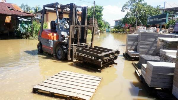 Pemandu forklif mengalihkan papan pelet di premis jualan jubinnya yang dinaiki air di Kampung Seberang Pendang semalam. -Foto Bernama