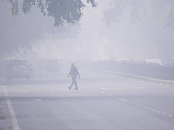 Seorang lelaki melintasi jalan raya di tengah-tengah jerebu beracun yang melanda New Delhi hari ini. - Foto: AFP