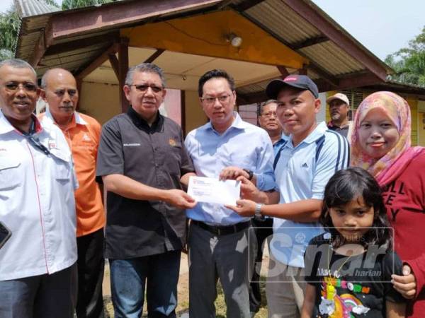 Salahuddin (tiga dari kiri), Jimmy (empat dari kiri) menyerahkan surat bantuan rumah kepada Abdul Rahman (dua dari kanan) di Kampung Serkat Laut, Pontian semalam.