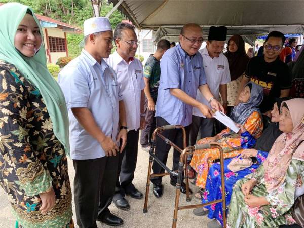 Abdul Aziz (empat dari kiri) menyampaikan zakat kepada Halimah Hassan, 81, sempena program Kasih Peladang Kelantan di PPK Lembah Pergau Kuala Balah di Jeli semalam.