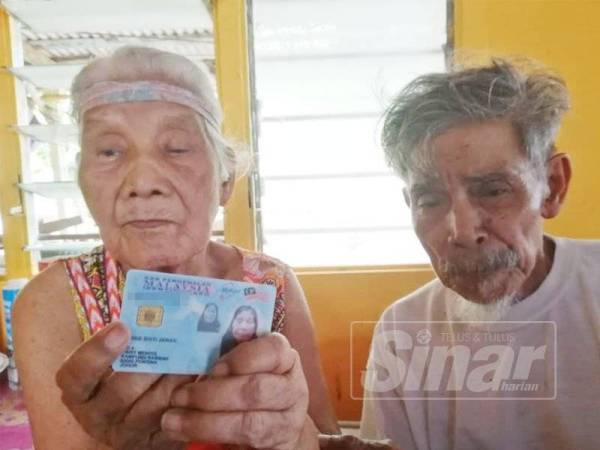 Jenab (kiri) menunjukkan MyKad sambil ditemani Salleh di rumahnya di Kampung Rambah, Pontian.