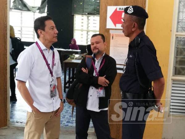 Azhar Azizan (kiri) berbual mesra dengan pegawai polis yang bertugas memantau keselamatan di pusat pengundian di SMK Dato' Mohd Yunos Sulaiman, Pekan Nanas hari ini.