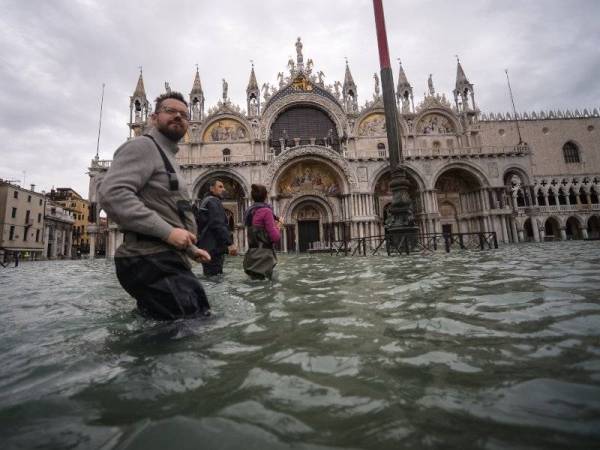 Orang ramai terpaksa meredah air yang membanjiri Dataran St Mark. - Foto: AFP