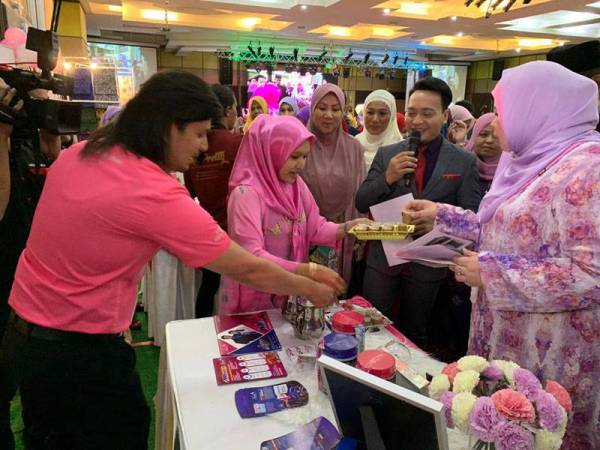 Rina (kanan) mencuba salah satu produk yang dipamerkan di WISE Kelantan di KTC hari ini.