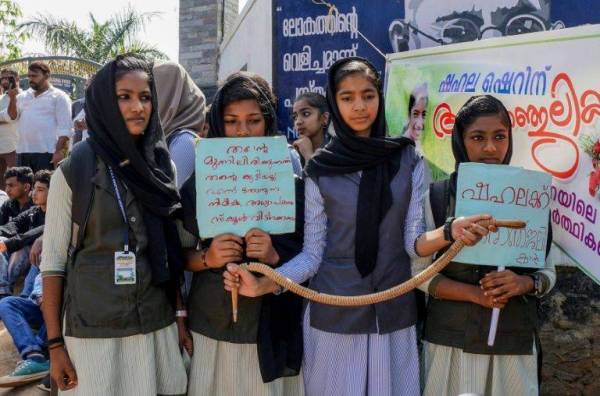 Pelajar sebuah sekolah di Kerala, India memegang plakad dan ular mainan ketika protes berhubung kematian pelajar berusia 10 tahun akibat dipatuk ular di dalam kelas. - Foto AFP