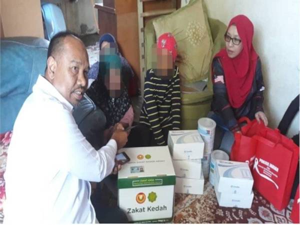 Muhammad Faidulatraf (kiri) menyerahkan Kit Bantuan Makanan Asasi LZNK dan wang ihsan kecemasan kepada Rushitta (dua dari kiri) sambil diperhatikan Zuraini (kanan) di Kampung Berjaya di sini.