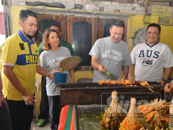 Andrew turut mencuba membakar sate ketika singgah di rumah seorang asnaf sambil diperhatikan Tuanku Syed Faizuddin.