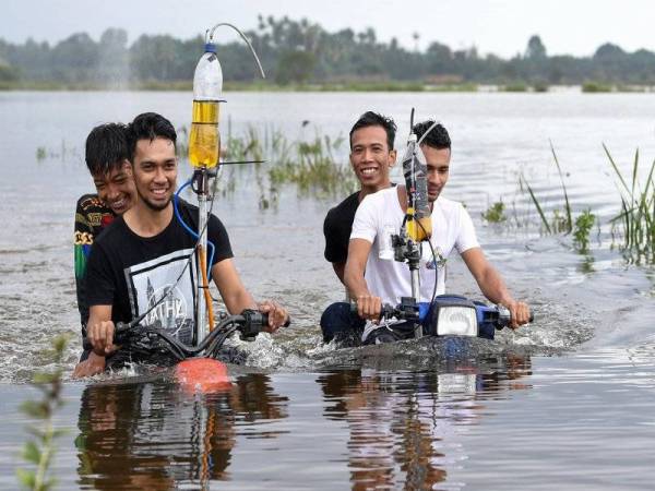 Muhammad Zakaria Mat Kail, 22, (kiri) dan abangnya Ikram Shahidi, 24, (kanan) menunggang motosikal telah diubahsuai yang mampu meredah banjir dengan lancar ketika ditemui di Kampung Banggol. - Foto Bernama
