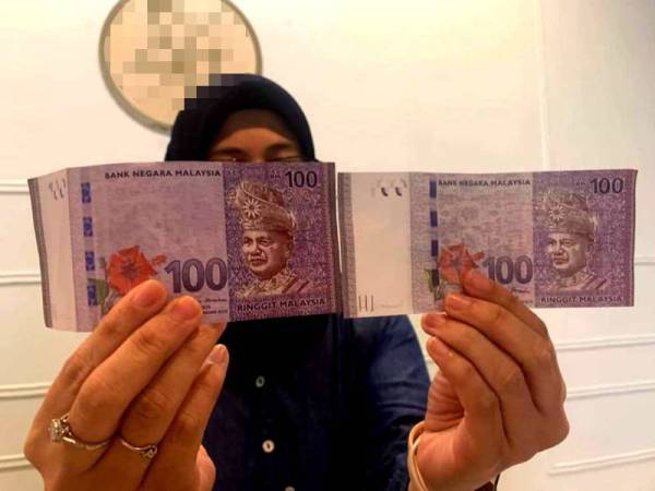 Nurul Nabihah menunjukkan perbandingan not kertas RM100 palsu diterima (kanan) dengan wang RM100 tulen.