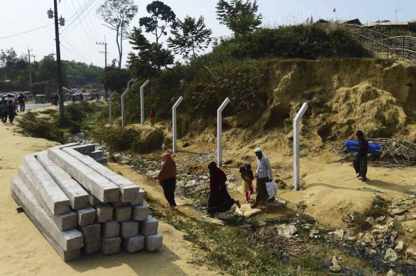 Pelarian Rohingya berjalan melewati tiang konkrit yang bakal dipasang di kem pelarian Balukhali di Ukhia. - Foto AFP