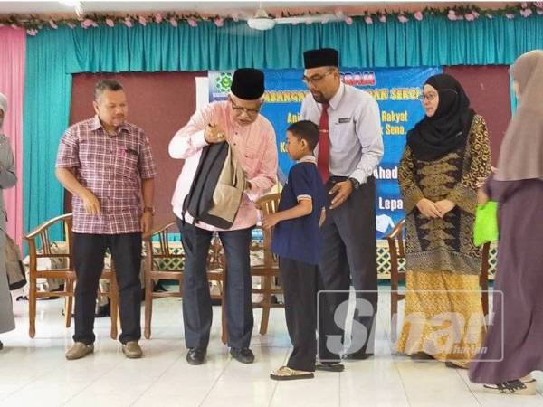 Mahfuz (dua dari kiri) menyampaikan kelengkapan sekolah kepada pelajar yang terpilih di Sekolah Kebangsaan Haji Abu Bakar, Lepai Bukit Pinang di sini hari ini.