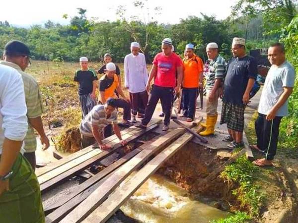 Sekumpulan penduduk bermandi peluh bergotong-royong menyiapkan 'jambatan' sementara di Kampung Gual Dalam apabila jalan utama di kampung tersebut runtuh akibat banjir.