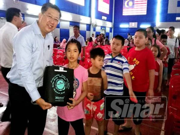 Kok Yew (kiri) mengagihkan sumbangan kit persekolahan kepada 200 pelajar sekolah di Dewan Komuniti Taman Nuri semalam.