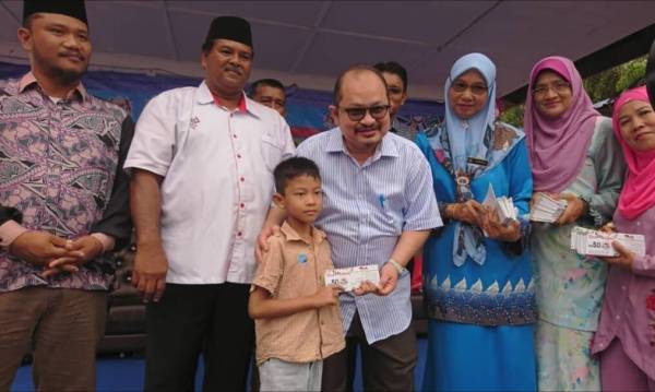 Shamsul Iskandar (tengah) mnyampaikan baucar kepada salah seorang penerima ketika program ‘Back To School’ anjuran Jawatankuasa dan Penyelarasan Dewan Undangan Negeri (JAPERUN) Rim di Kompleks JAPERUN Rim, Bandar Baru Jasin di sini hari ini.