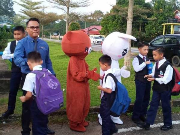 Murid-murid bersalam dengan maskot dan guru yang menyambut kehadiran mereka pada hari pertama persekolahan.