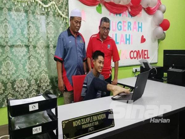 Zulkifle menggunakan kakinya untuk melaksanakan tugasnya sebagai Pegawai ICT di Pusat Khidmat DUN Paloh, Gua Musang sambil diperhatikan oleh Azman (kiri).