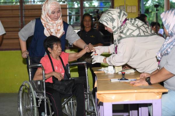 Lucine Matajil, 69, dibantu oleh Petugas SPR mencelup jari ke dalam botol dakwat ketika mengundi pada PKR Parlimen Kimanis di Sekolah Kebangsaan Our Lady of Fatima (M) Kelatuan hari ini. - Foto: Bernama
