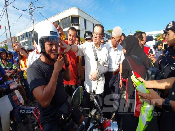 Guan Eng (tengah) memberi topi keledar baharu kepada seorang penunggang motosikal sempena kempen keselamatan jalan raya pagi tadi.
