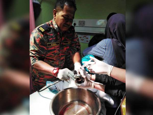 Anggota bomba mengeluarkan ibu jari tangan kanak-kanak terbabit yang tersangkut pada tombol pintu. -Foto Bomba