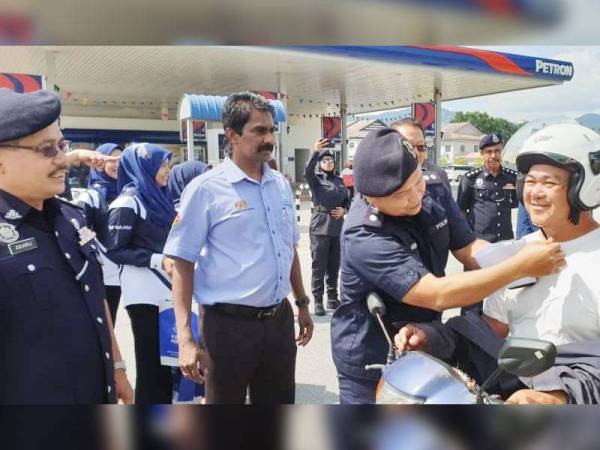 Pada kempen 'jom klik', Ahmad Adnan memasang topi keledar kepada salah seorang penunggang motosikal di Pusing semalam.