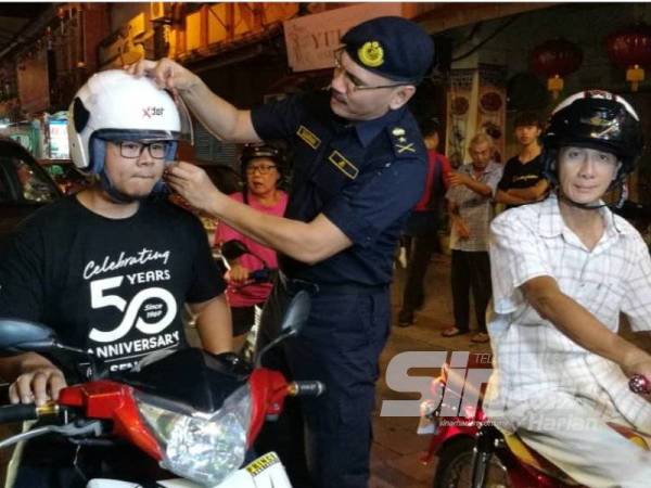 Zulkarnain memakaikan topi keledar yang diberikan kepada salah seorang pengguna jalan raya di Jalan Kampung Cina di sini sempena pelancaran Ops Tahun Baru Cina 2020 Peringkat JPJ Terengganu malam tadi.