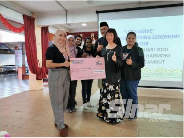 Doktor Nasuha (kiri) dan penggerak program Let’s Serve menyampaikan replika cek bernilai RM1,000 kepada pengetua SMK Segambut sempena majlis penutupan program.