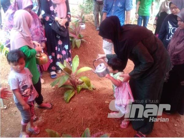 Nurul Azmira bersama salah seorang anaknya menyirami pusara arwah suaminya hari ini.