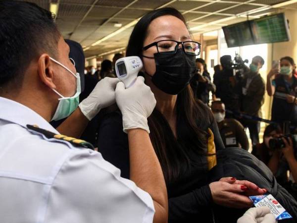 Seorang pekerja kesihatan menggunakan termometer inframerah untuk memeriksa suhu pelancong yang tiba di Lapangan Terbang Don Mueang, Thailand. - Foto Reuters