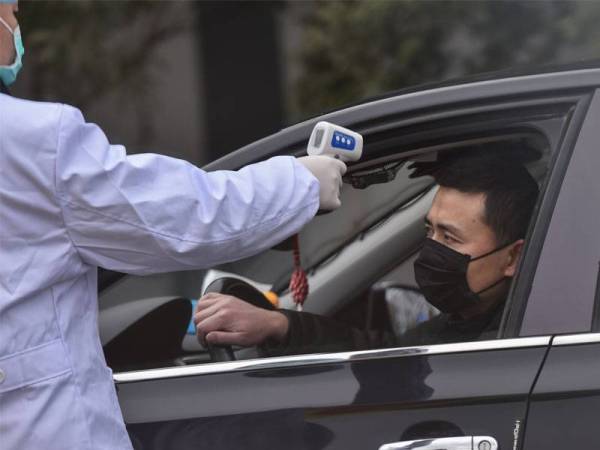 Seorang polis mengambil suhu seorang pemandu di sebuah pusat pemeriksaan di pinggir Wuhan, China. - Foto AFP