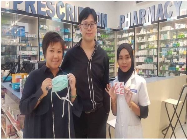 Esther (kiri) dan kakitangan Just Pharmacy menunjukkan topeng muka dan swab alkohol yang dibekalkan secara percuma kepada pengguna.