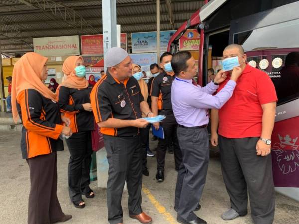 Dr Mohd Azman (dua dari kanan) diperhatikan Laili (tengah) memakaikan topeng muka dengan betul kepada salah seorang penumpang Ekspres Perdana.