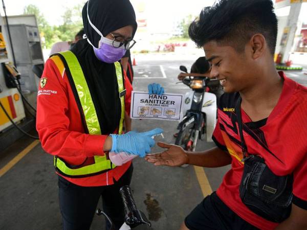 Penyelia stesen minyak di Jalan Sultan Tengah di Petra Jaya, Kuching, Sharifah Nurul Fatihah (kiri) menyembur cecair pembasmi kuman (hand sanitizer) pada tangan seorang pelanggan. -Foto Bernama