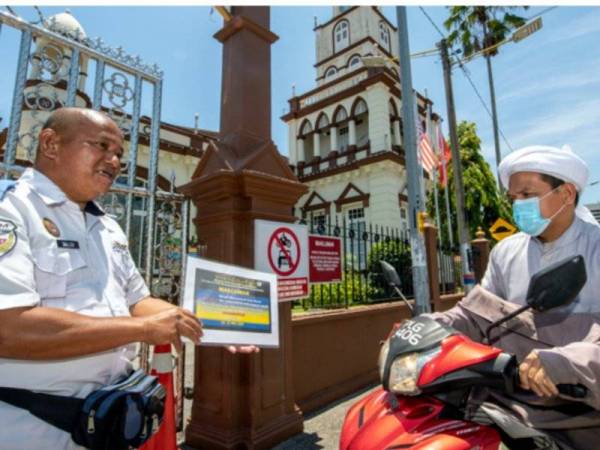 Pengawal keselamatan Masjid negeri di Masjid Muhammadi, Kota Bharu, Salleh Musa,51, (kiri) menunjukkan notis pemberitahuan Solat Jumaat ditangguhkan kepada salah seorang kariah masjid yang ingin menunaikan Solat Jumaat di pintu masuk di Masjid Muhammadi hari ini. Foto: Bernama