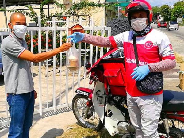 Pekerja penghantar makanan memakai topeng muka, sarung tangan serta cecair pencuci tangan semasa menghantar pesanan kepada pelanggan.