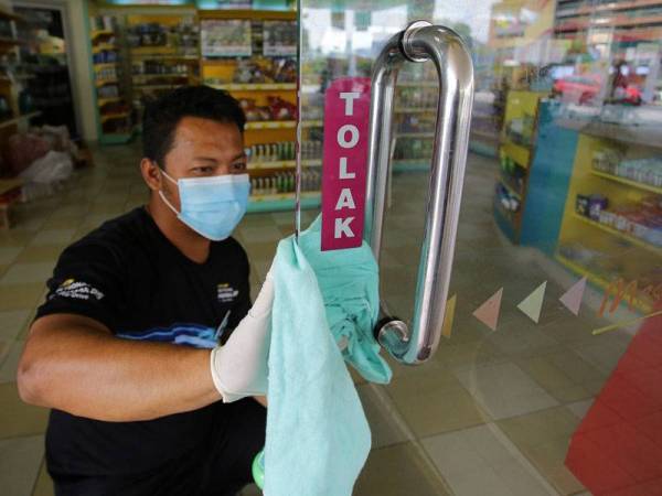 Kakitangan stesen minyak Mohd Saiful Rizal Abd Ghani melakukan kerja-kerja pembersihan pada pemegang pintu masuk di stesen itu sebagai langkah-langkah pencegahan penularan Covid-19. -Foto Bernama