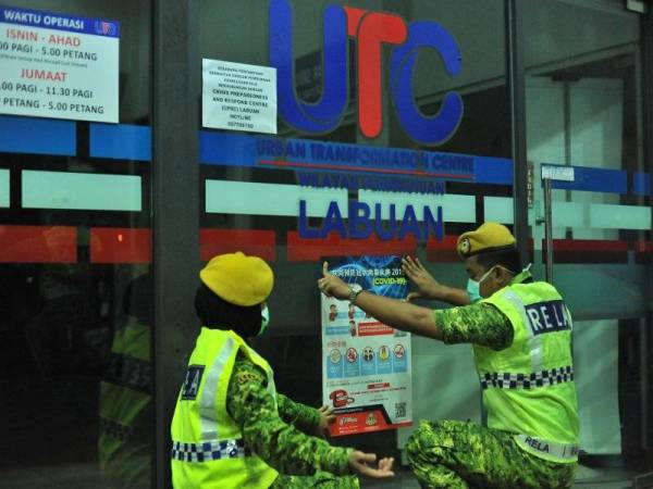 Anggota Rela Wilayah Persekutuan Labuan meletakkan poster pencegahan Covid-19 di Terminal Feri Antarabangsa Labuan. -Foto Bernama