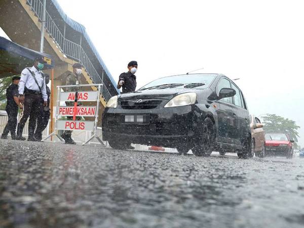 Biarpun hujan lebat anggota polis yang dibantu anggota tentera tetap menjalankan sekatan jalan raya susulan Perintah Kawalan Pergerakan. -Foto Bernama