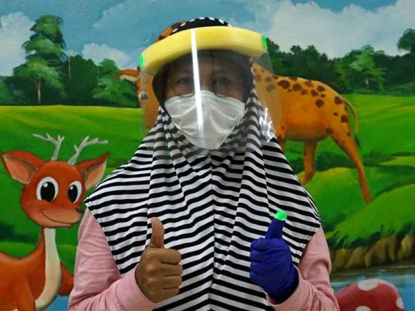 Pemilik Tadika Bestari Genius Salmiah Ahmad memakai perisai muka buatan sendiri (DIY) yang dihasilkannya untuk kegunaan barisan hadapan di Klinik Kesihatan Kuah. -Foto Bernama