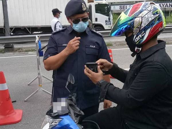 Arifai sedang menyoal seorang penunggang motosikal di sekatan jalan raya di Kilometer 14 Jalan Ipoh, di sini, hari ini.