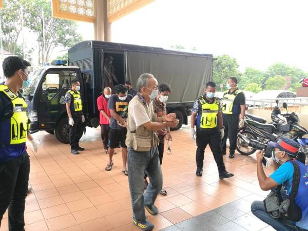 Lelaki warga Jepun (depan) bersama 10 yang lain diiringi anggota polis ketika dibawa ke Mahkamah Majistret di sini hari ini untuk sebutan kes langgar PKP.