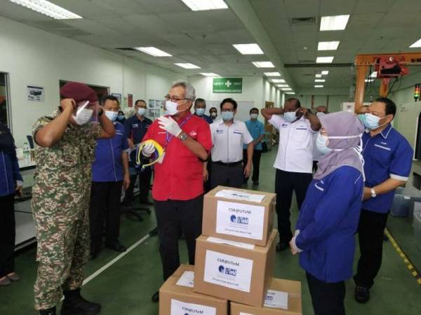 Mohd Redzuan (tengah) melihat bagaimana cara pemakaian pelindung muka yang dihasilakan UTeM untuk para frontliners.