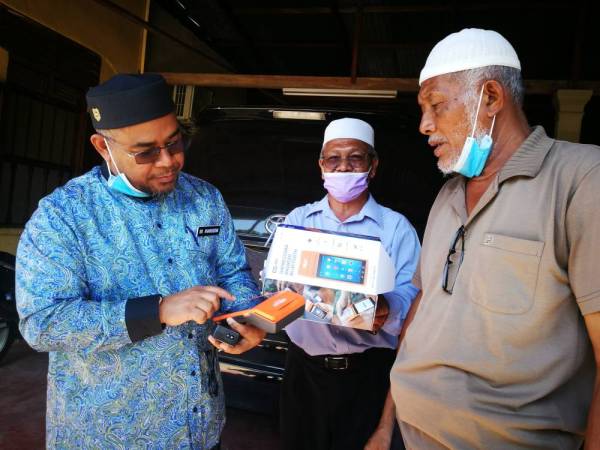 Mohd Khairuddin (kiri) bersama Mohd Habali (kanan) dan Abdul Nasir melihat alat pengesahan yang boleh membantu penoreh memasukkan data dan rekod penjualan getah.