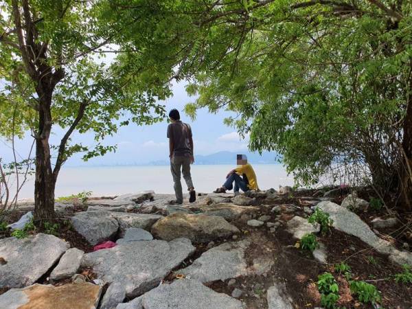 Dua lelaki dikesan sedang melepak di tepi laut.