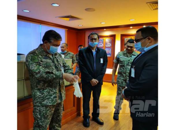 Ahmad Hasbullah (kiri) mencuba sarung tangan dan topeng muka yang disumbangkan pihak Bank Rakyat hari ini.