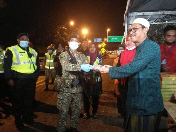 Ahmad Faizal (kanan) menyampaikan makanan sahur kepada petugas barisan hadapan ketika melawat sekatan jalan raya berhampiran plaza tol Jelapang, di sini malam tadi.