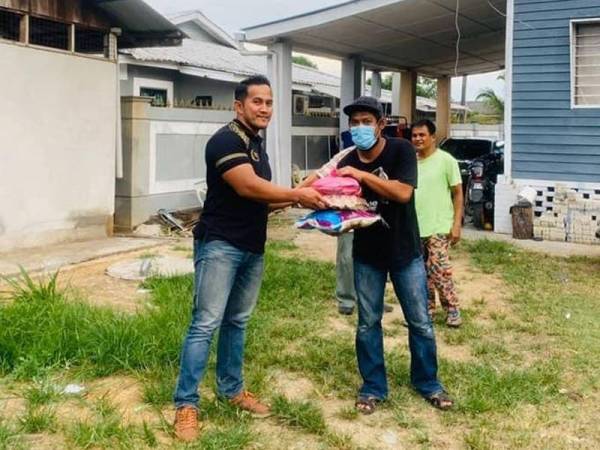 Tengku Shah Rizal (kiri) menyampaikan sumbangan ikan segar dan barangan keperluan harian kepada salah seorang penerima.